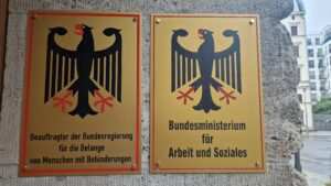 Schilder mit dem Bundesadler am Eingang des BMAS: links: schwarzer Adler auf gelbem Hintergrund mit dem Schriftzug 